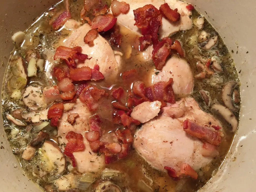 Over head view of the chicken. broth, mushrooms and bacon in a pan