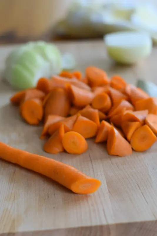Chopped triangles of carrots on a board with a cut onion in the background