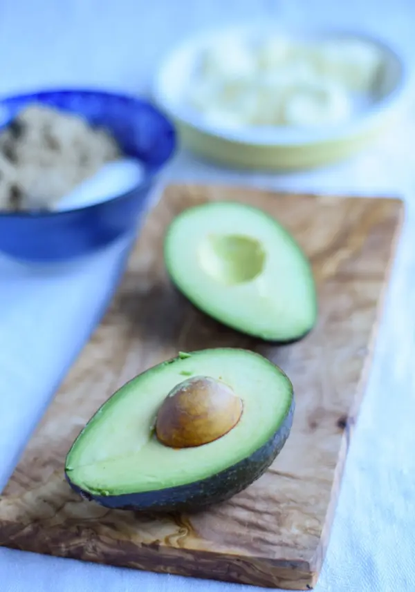 Avocado cut in half on a wooden board, with other ingredients in the background
