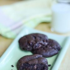 Dark chocolate cookies on a green rectangle plate with milk and more cookies in the background