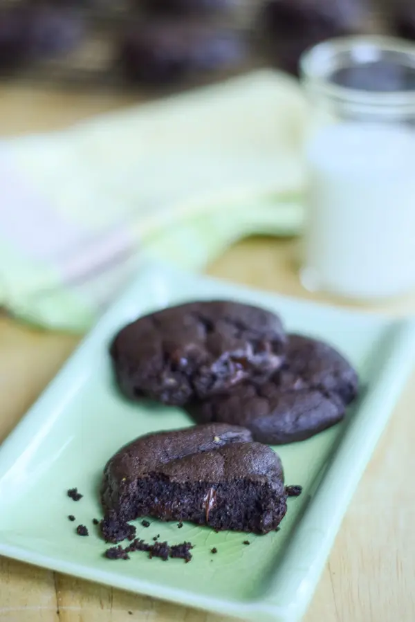 Dark chocolate cookies on a green rectangle plate with milk and more cookies in the background