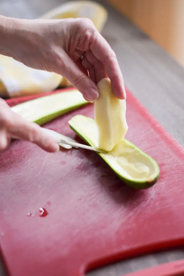 A woman's hand cutting into a zucchini cut lengthwise and removing the flesh