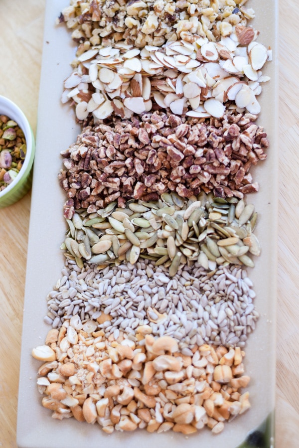 Overhead view of pistachio nuts next to a rectangular plate covered with nuts and seeds