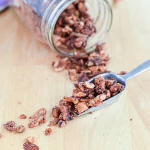 A scoop with granola spilling off it with a jar on it's side behind it