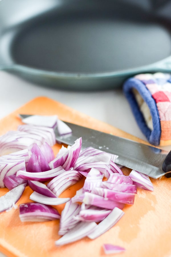 Purple onion cut up on a orange board and a saut&eacute; pan in the background