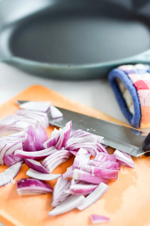 Purple onion cut up on a orange board and a sauté pan in the background