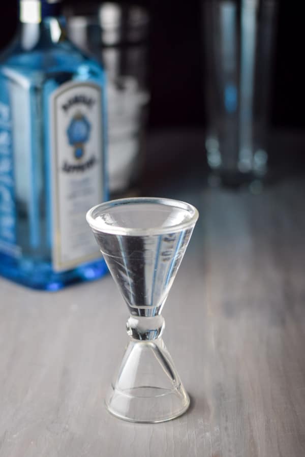 Gin poured out with the bottle, shaker and glass in the background