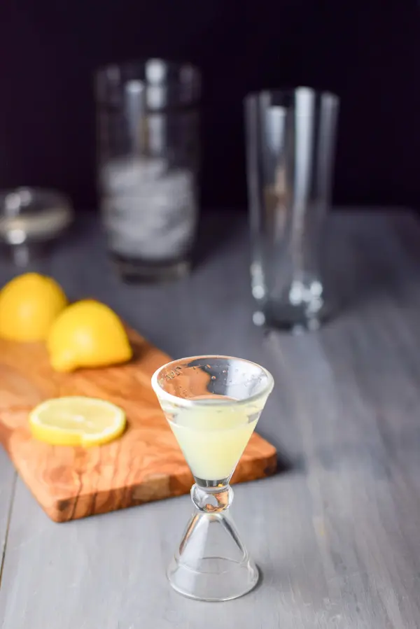lemon measured out with a wooden board with cut lemons. There is a cocktail shaker and glass in the background