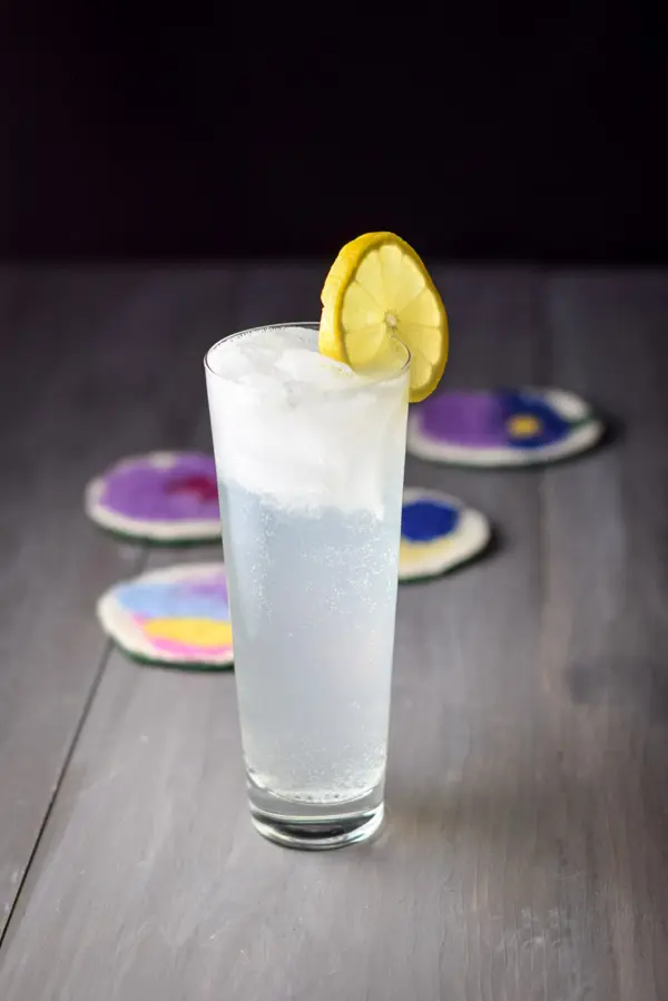 The flared glass filled with the cocktail with a lemon wheel on the glass rim