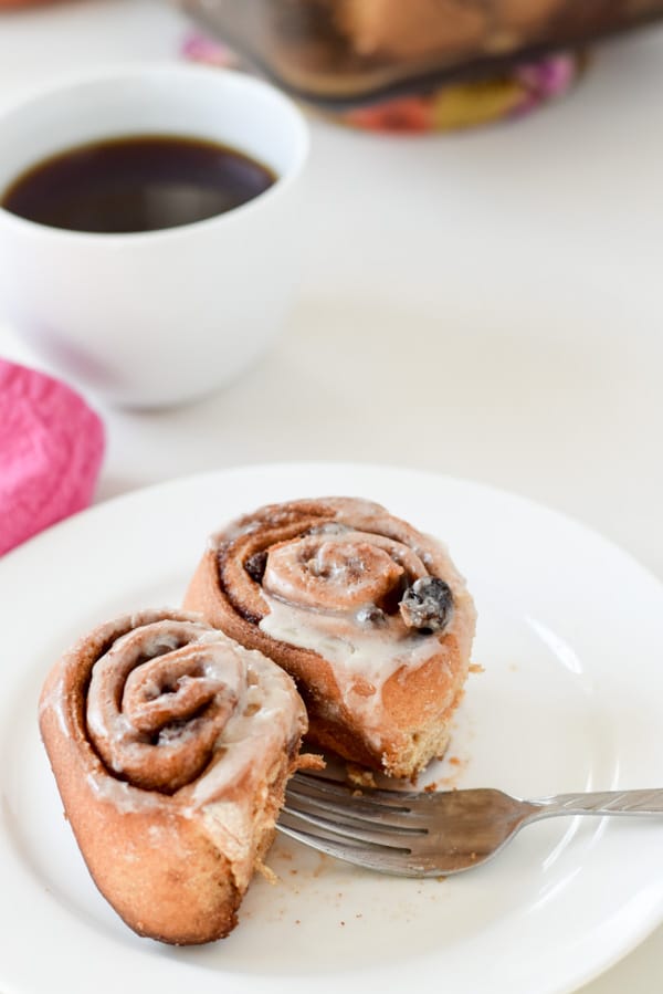 Two rolls on a white plate with some coffee in the background