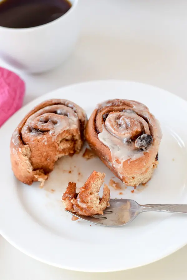 Two cinnamon rolls on a white plate with a bite taken out and on a fork