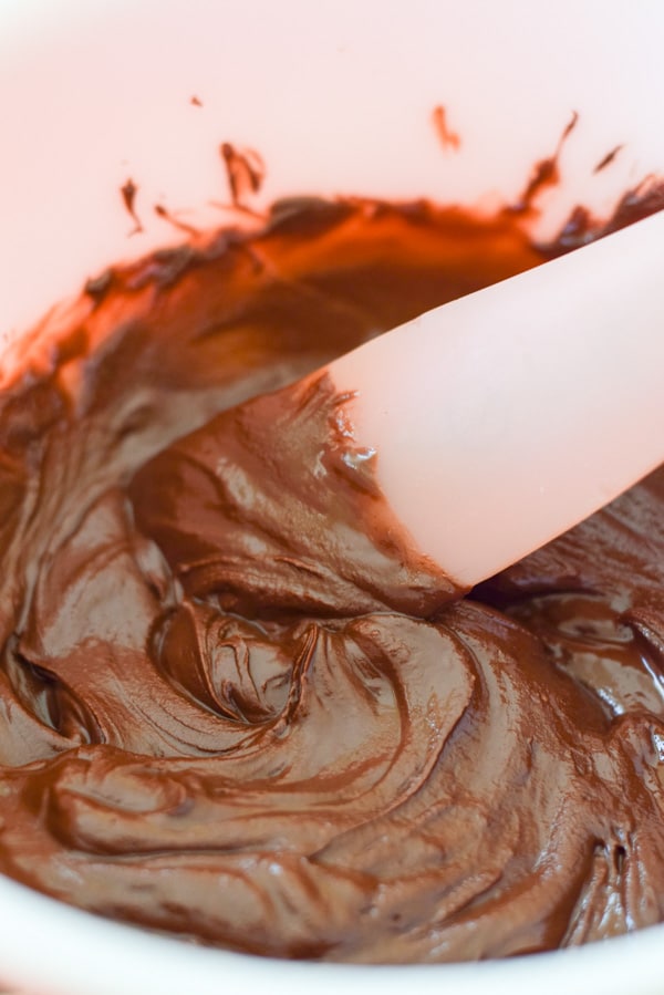 Close up of the rubber spatula stirring the melted dark chocolate for dipping the candies into.