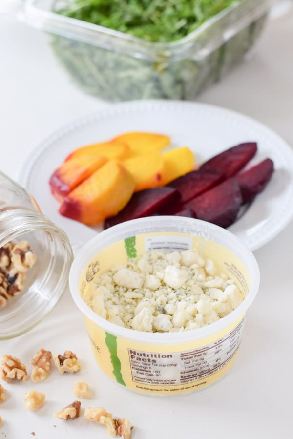 Cheese, walnut pieces, cooked and sliced beets, and container of arugula leaves.