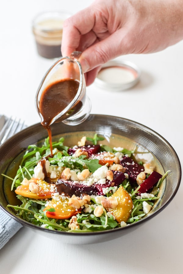 Hand pouring slowly from above a small pitcher of balsamic vinaigrette dressing over the beet salad.