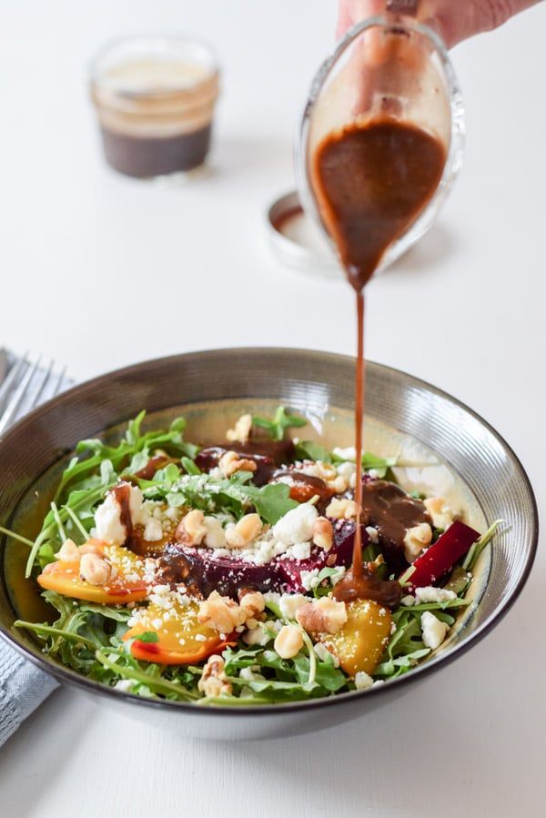 Hand pouring slowly from above a stream of balsamic vinaigrette dressing onto the salad.