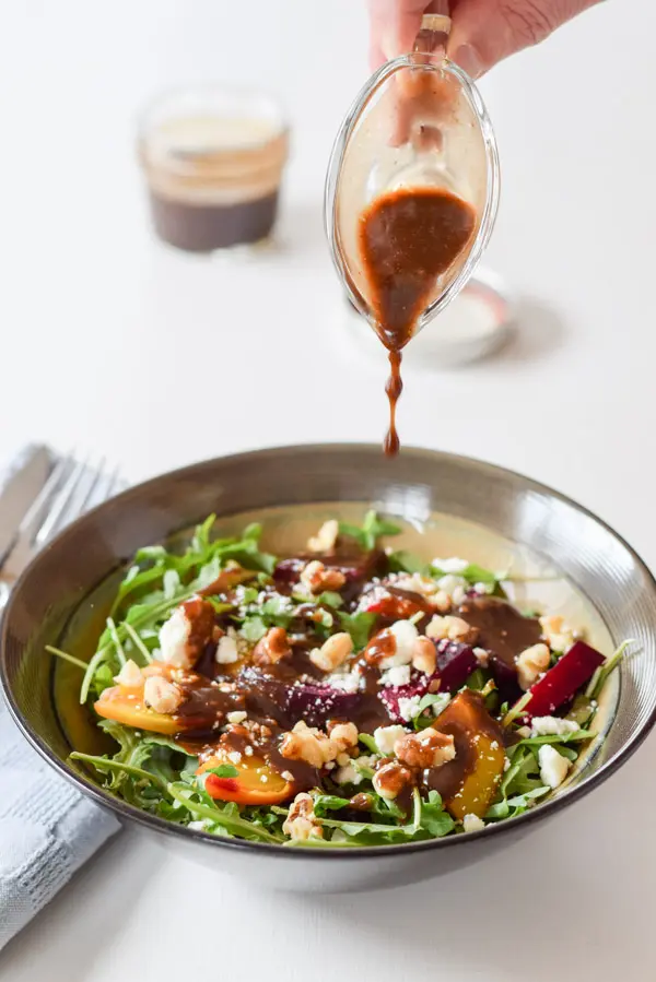 Hand pouring slowly from higher above a last few drops of balsamic vinaigrette dressing onto the salad.