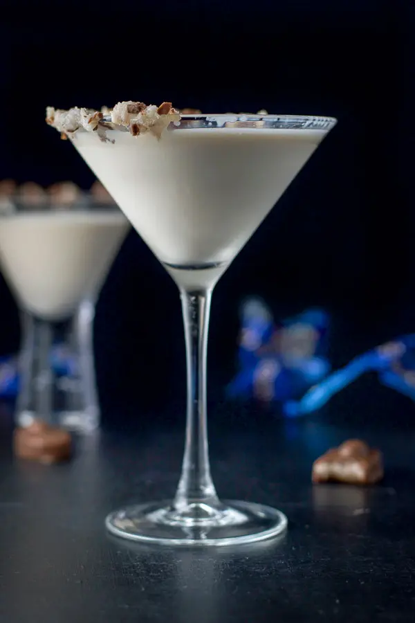 Vertical view of the tall martini glass with the delicious creamy drink in it and smooshed candy bars on the rim