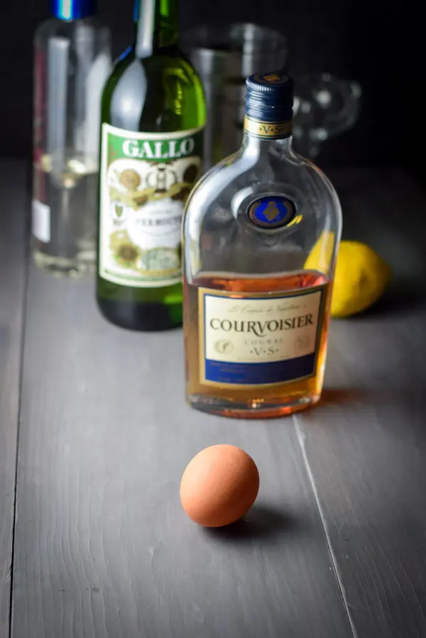 Egg, cognac, dry vermouth, simple syrup, glass and shaker on a grey table