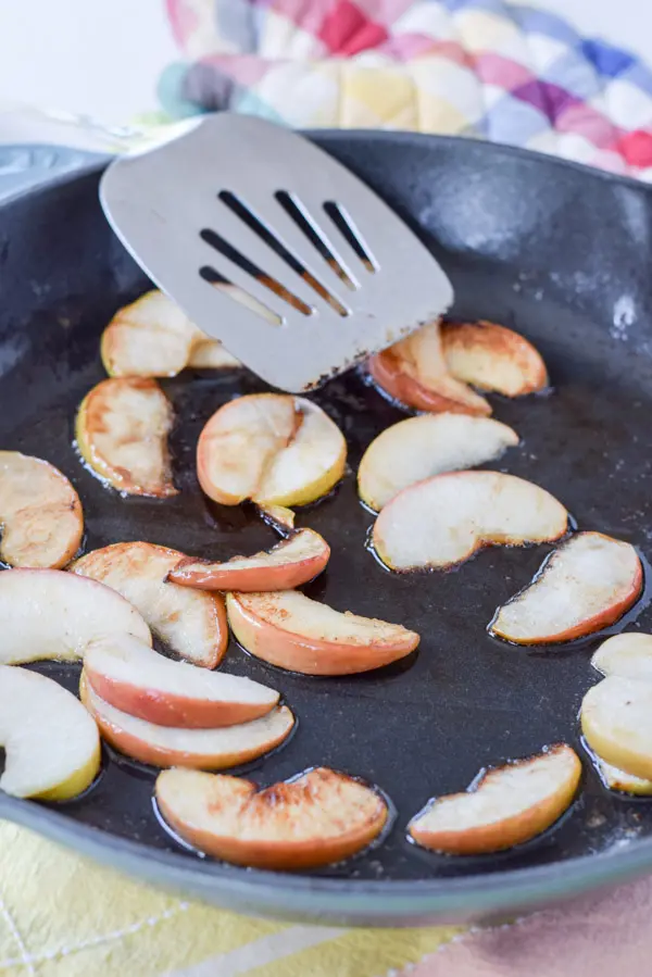 Apples sautéed in a cast iron skillet with a metal spatula