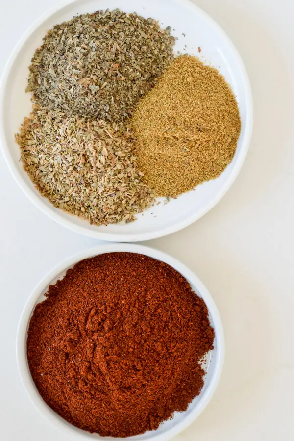 Chili powder, cumin, basil and oregano in small white dishes