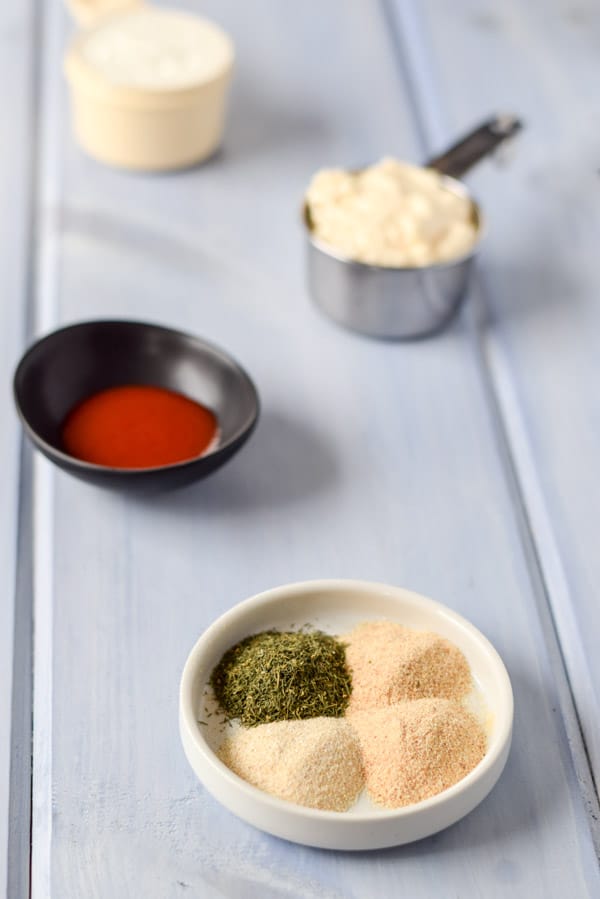 Garlic and onion powder and herbs in a white plate with sriracha sauce, mayo and yogurt