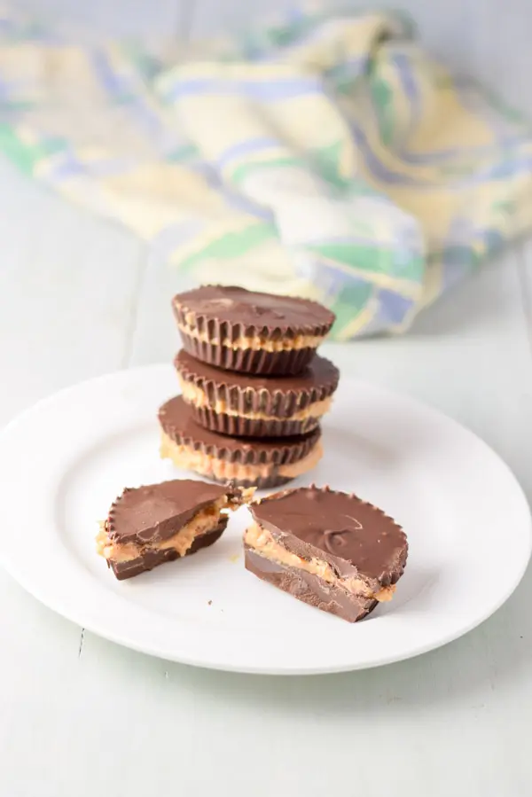 A white plate with a split peanut butter cup and three other cups in a stack