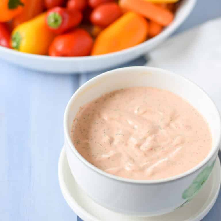 The dipping sauce in a white bowl with vegetables in the background - square