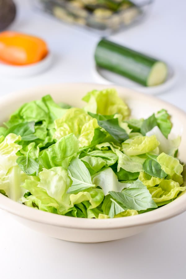 Lettuce torn in a beige bowl with the rest of veggies in the background