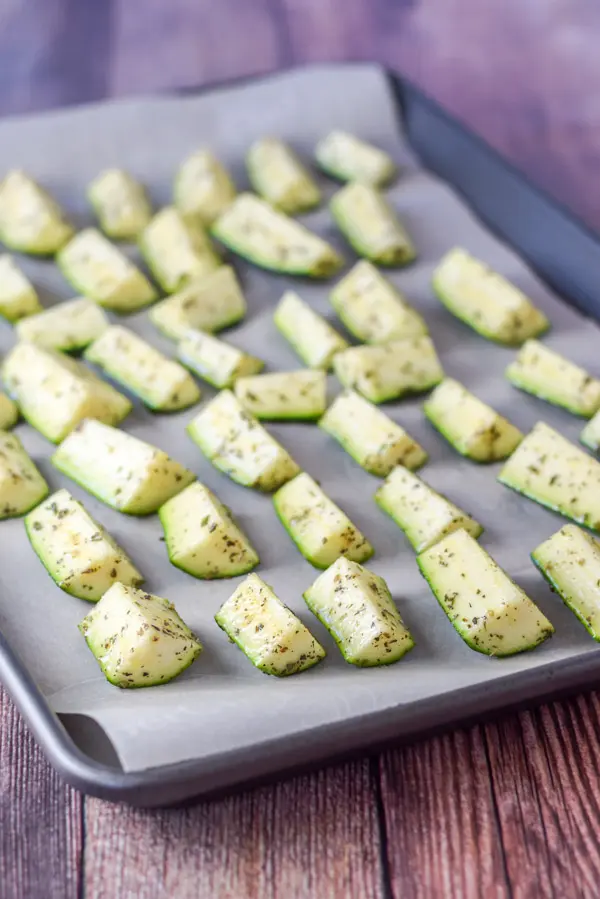 Herb coated zucchini lined up on a jelly roll pan