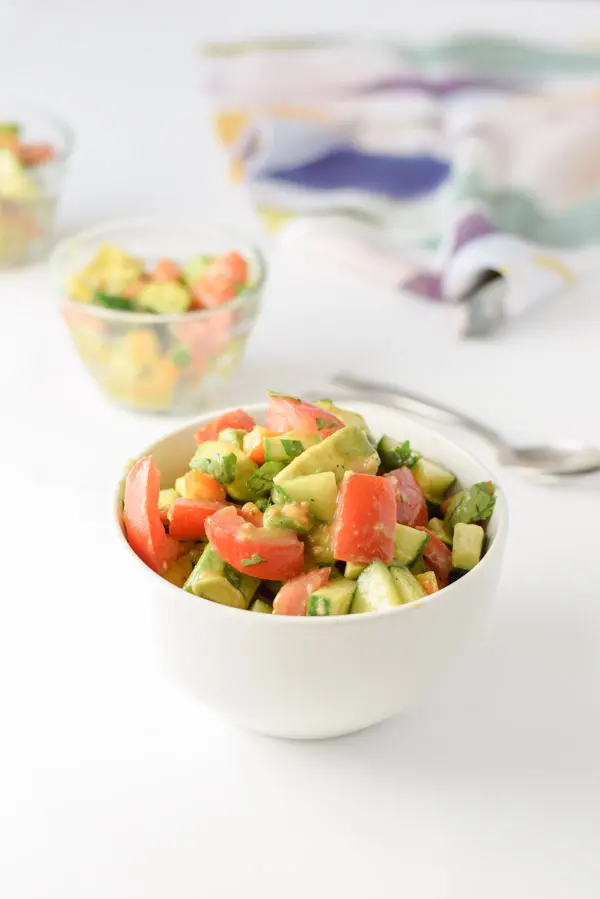 A small bowl filled with avocado tomato salad with a few more bowls and a napkin in the background
