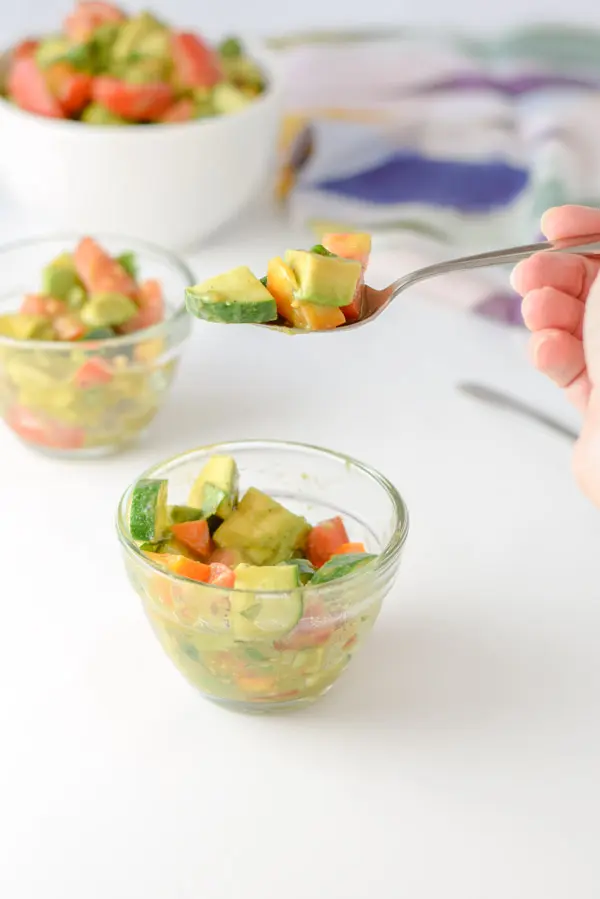A forkful of of avocados, cucumber and tomatoes held over a bowl with more of the salad in it