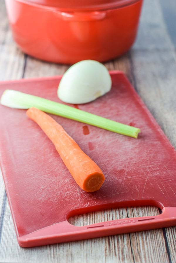 Carrot, celery and onion on a red cutting board and a Dutch oven in the background