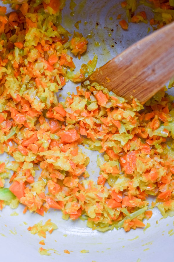 Overhead view of onion, carrot and celery saut&eacute;ed in a pan with a wooden spatula in it