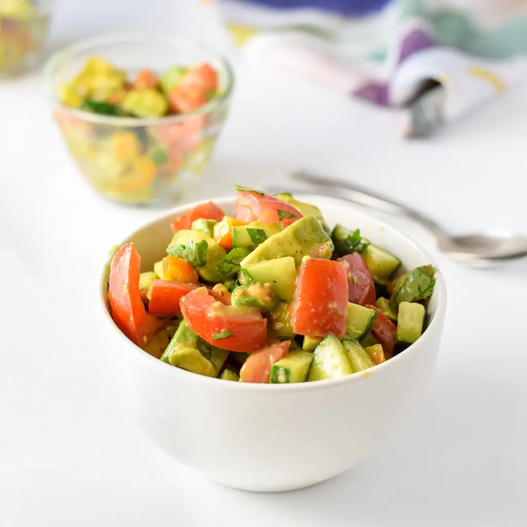 A white bowl filled with avocados, tomatoes and more vegetables, with a few smaller bowls in the background