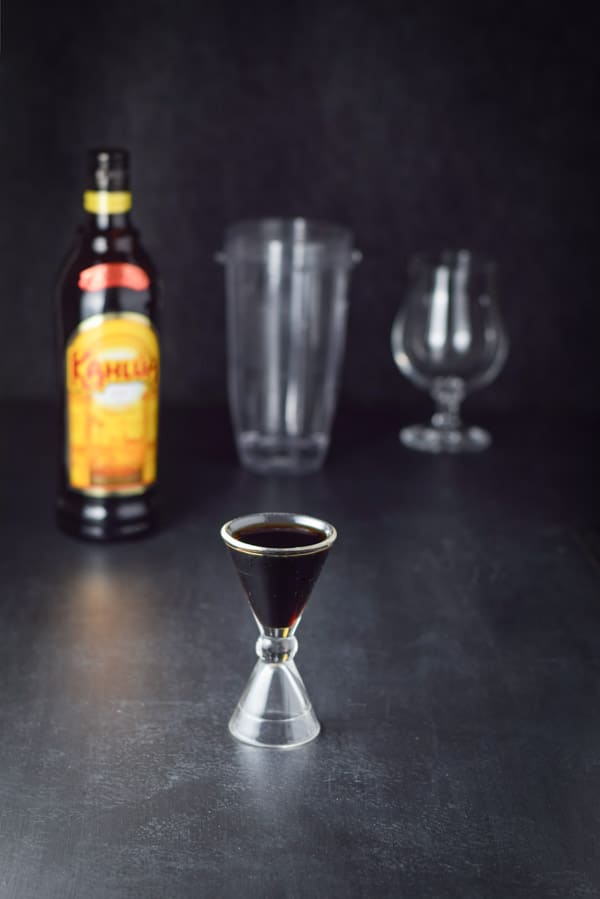 Kahl&uacute;a measured out with the bottle, container and glass in the background