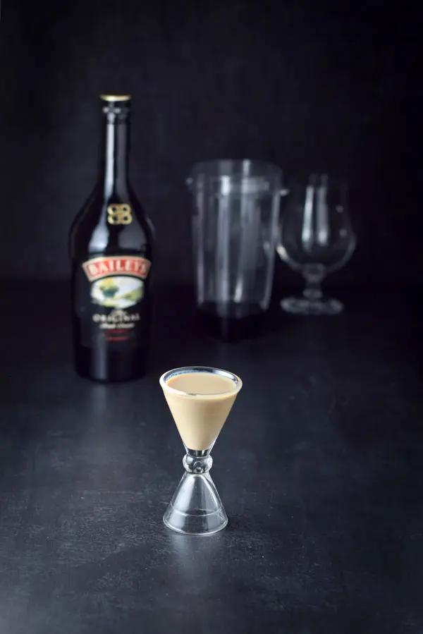 Irish cream measured out with the bottle, container and tulip glass in the background