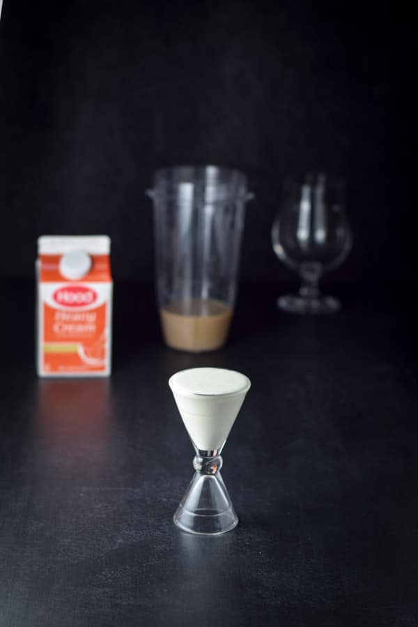Heavy cream measured out with the containers and tulip glass in the background