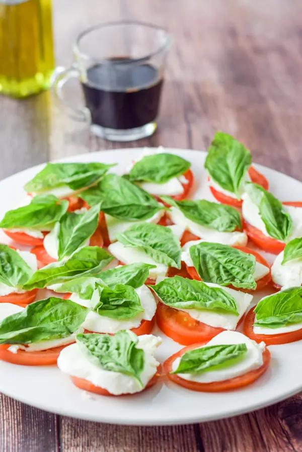 Basil on the cheese and tomato slices with oil and vinegar in the background