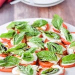 White plate with the tomato, basil and cheese salad with two other places in the background