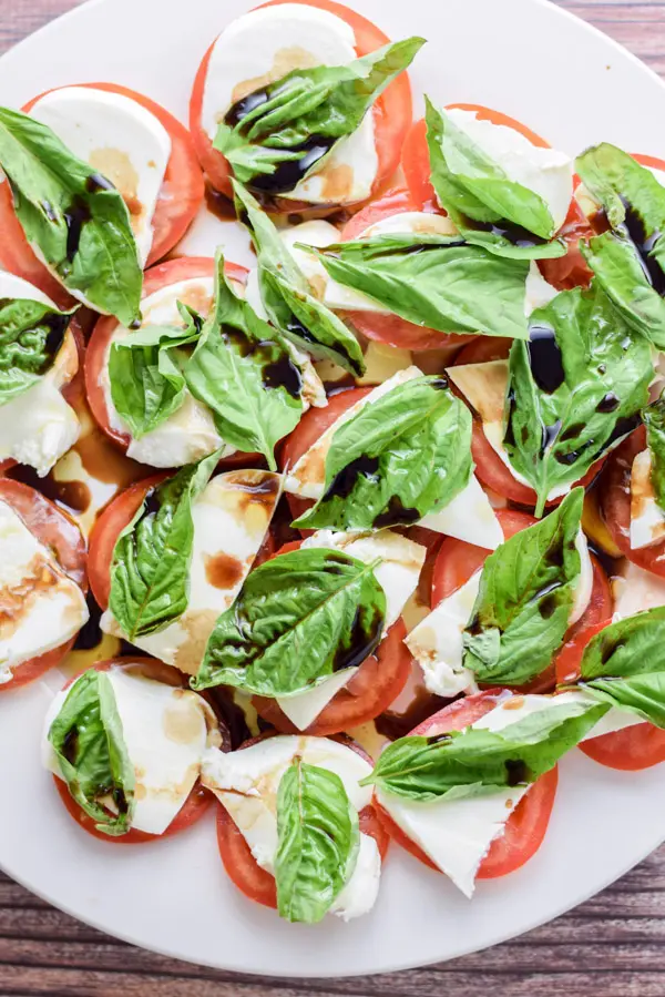 Overhead view of a round white plate with tomato slices with cheese, basil and balsamic vinegar