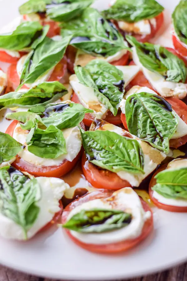 A white plate with tomatoes topped with cheese, basil and balsamic vinegar
