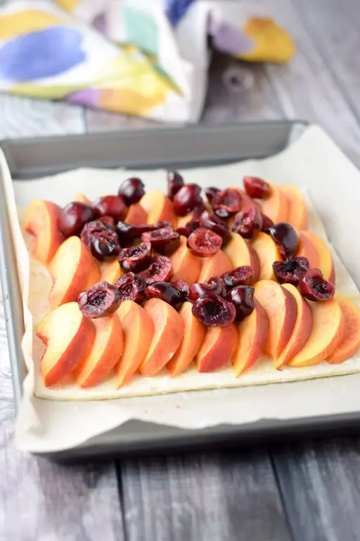 Peaches lined up on puff pastry with cherries sprinkled on top