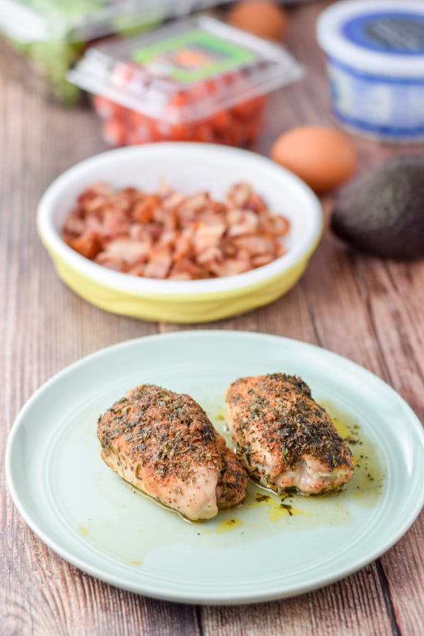 A green plate with herb chicken, bacon, avocado, eggs, cheese, tomatoes and lettuce on a table
