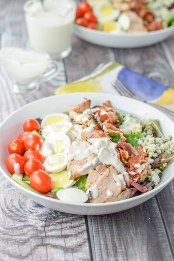 Blue cheese dressing fully poured onto the colorful lined salad with another bowl in the background as well as the dressing in containers