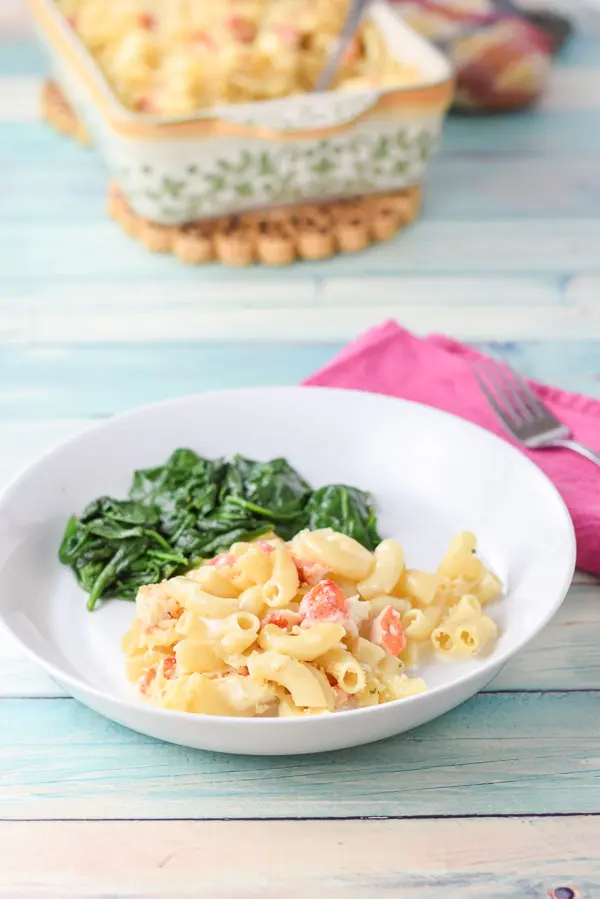 A white shallow bowl with the macaroni and spinach with the baking dish of the lobster in the background