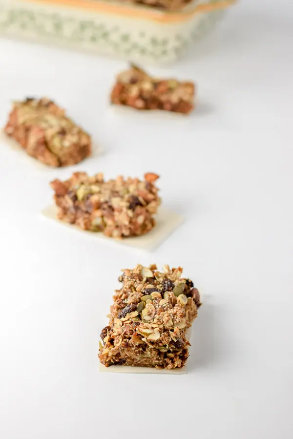 Rectangles cut up into granola bars. There are four of them on the table with the baking pan in the background