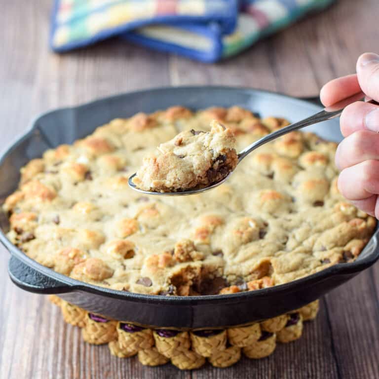 A spoonful of the chocolate chip cookie hovering over a pan fresh out of the oven