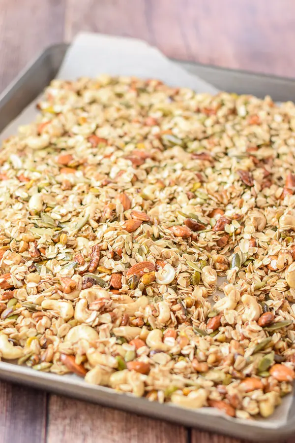 A parchment paper lined jelly roll pan with raw granola spread on it