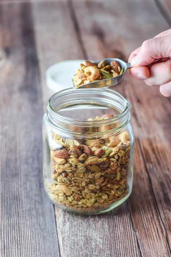 A hand holding a scoop of granola over the jar