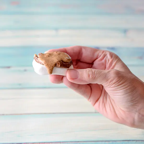 A woman's hand holding a flat marshmallow with Nutella and almond butter on it